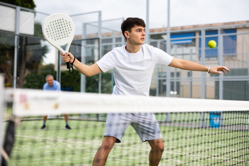 Emotionaler junger Mann spielt Padel-Tennis auf offenem Platz