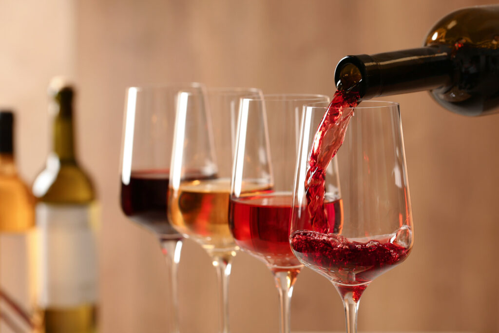Einschenken von Wein aus der Flasche in ein Glas vor unscharfem Hintergrund, nah